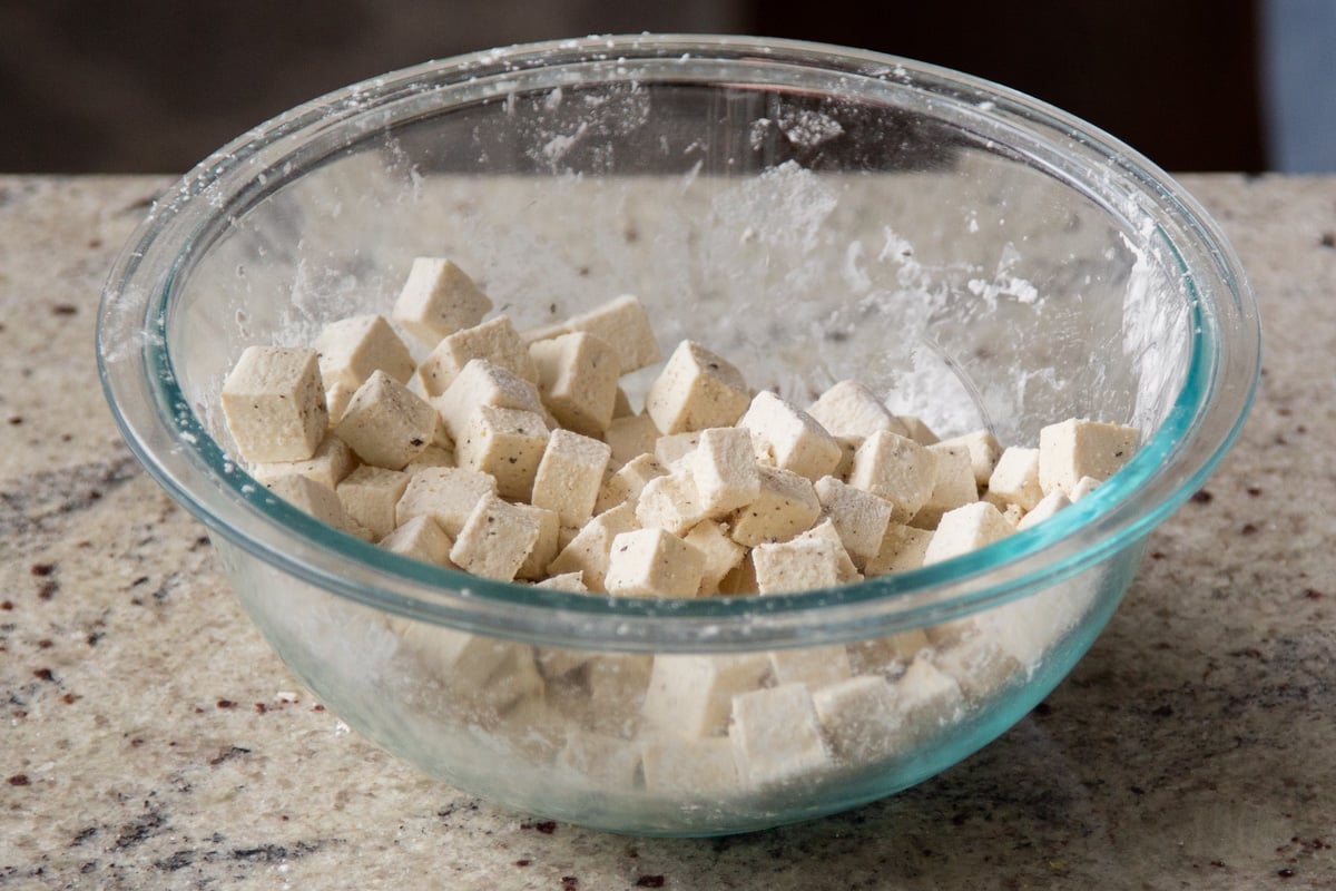 cubed tofu coated in cornstarch in a glass bowl