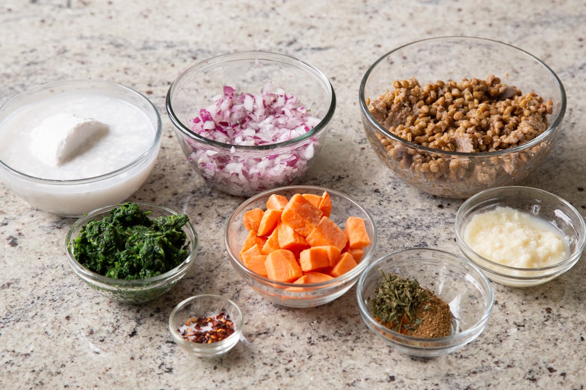 lentils, sweet potatoes, coconut milk, and other curry ingredients in bowls on a kitchen counter