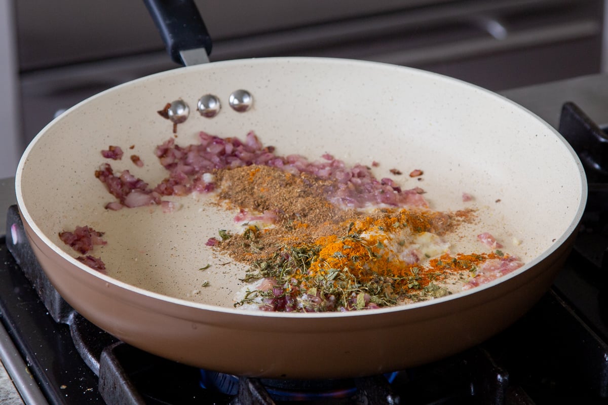 adding dried spices to the pan with cooked onion, ginger, and garlic