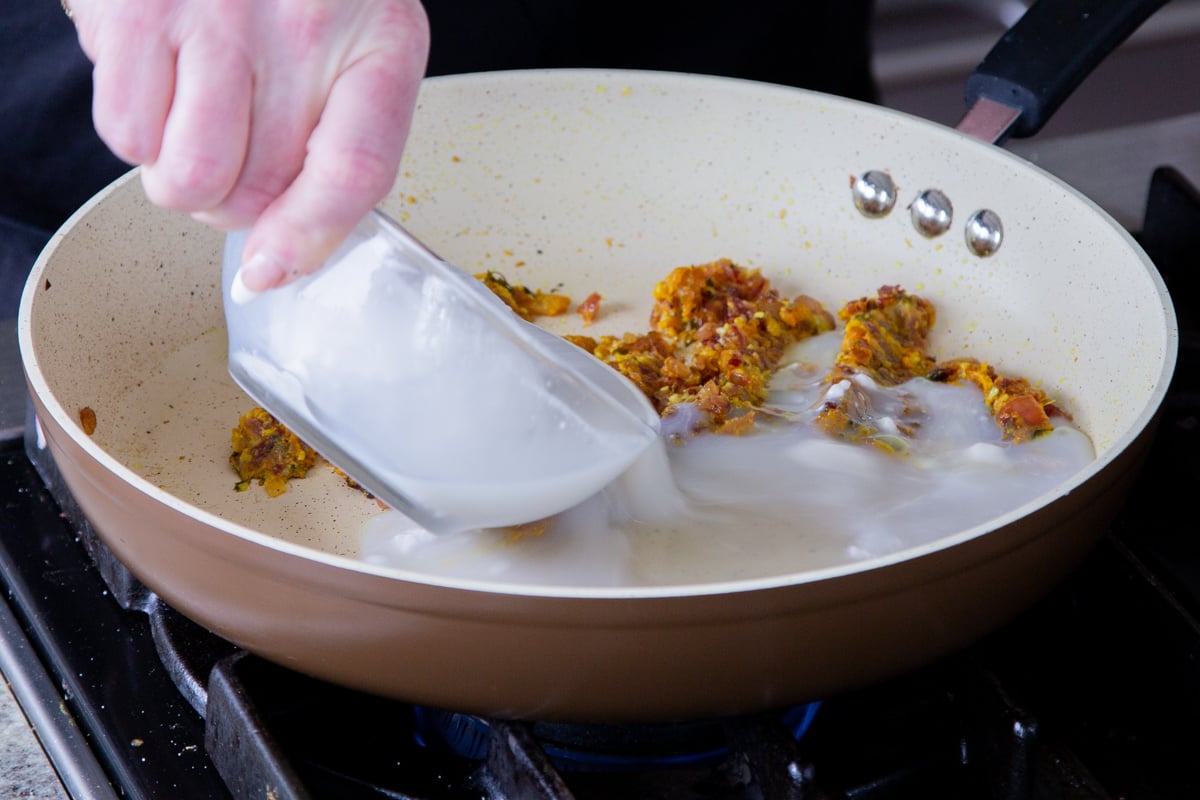 adding coconut milk to the onion mixture in the pan