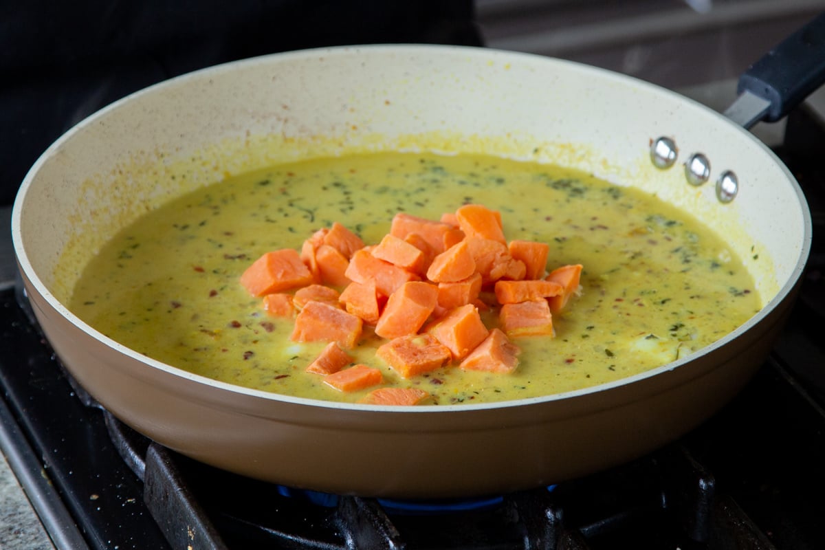 adding sweet potatoes to the coconut curry sauce in the pan