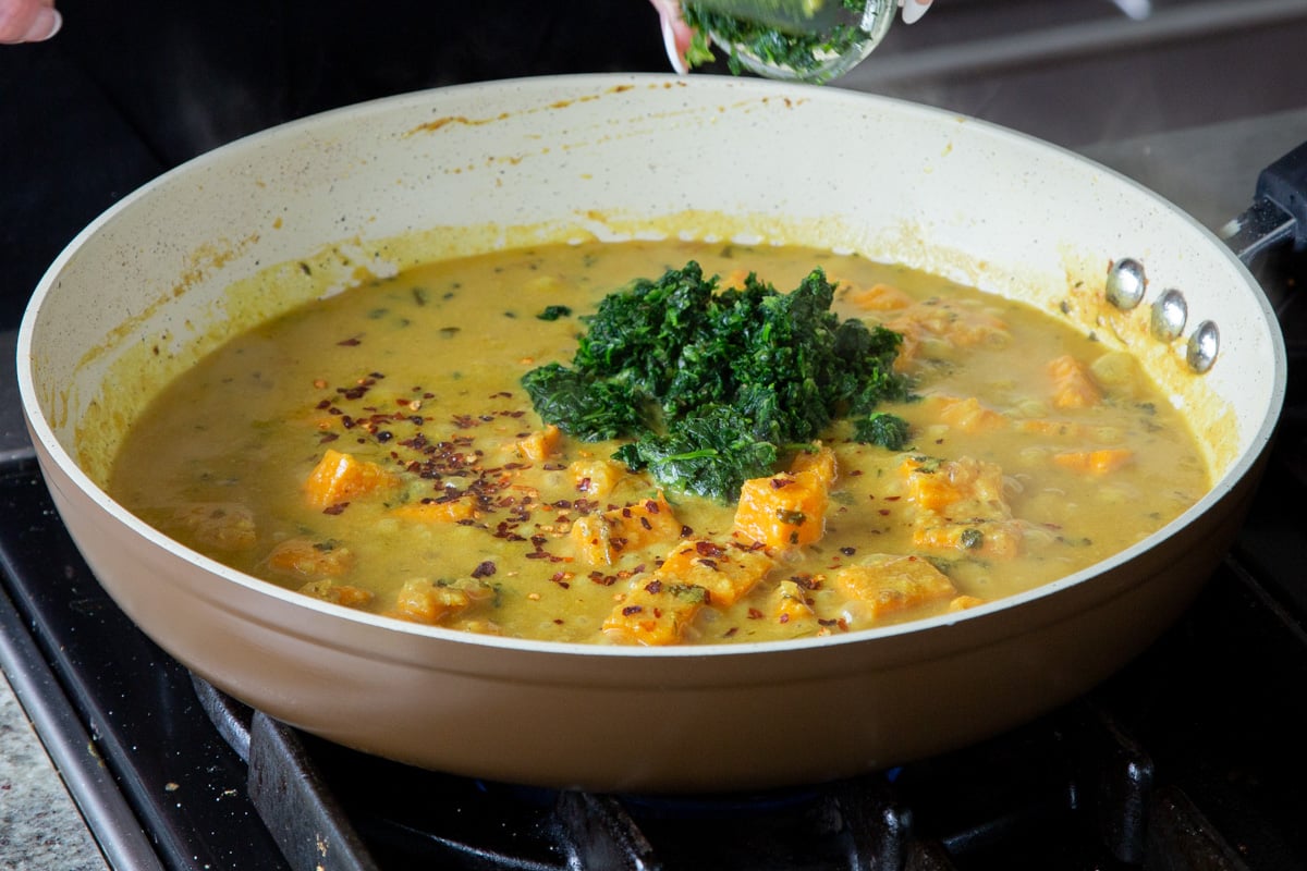 adding spinach to the cooked sweet potato in the pan