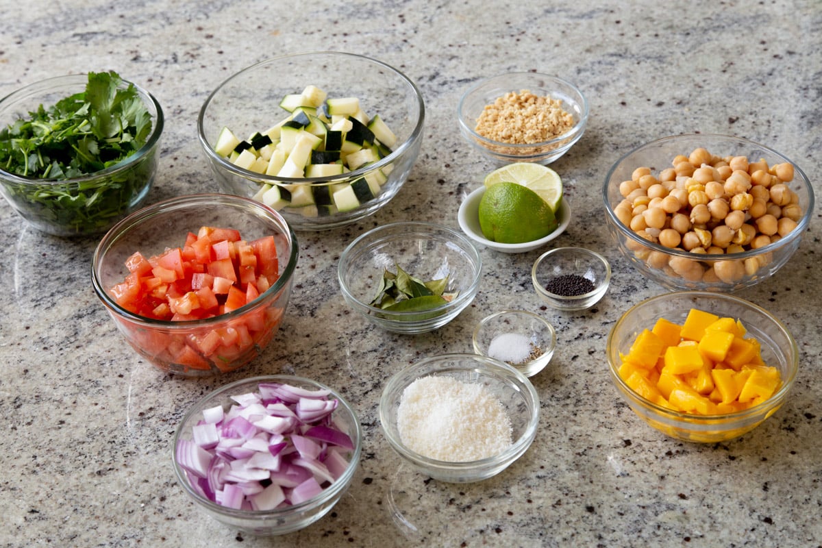 veggies, fruit, chickpeas, and seasonings in bowls on a kitchen counter