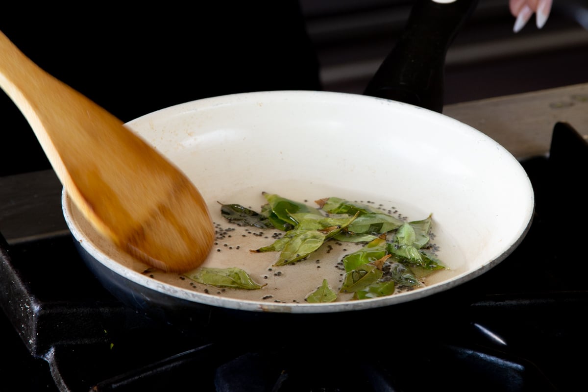 adding curry leaves to the pan with the mustard seeds