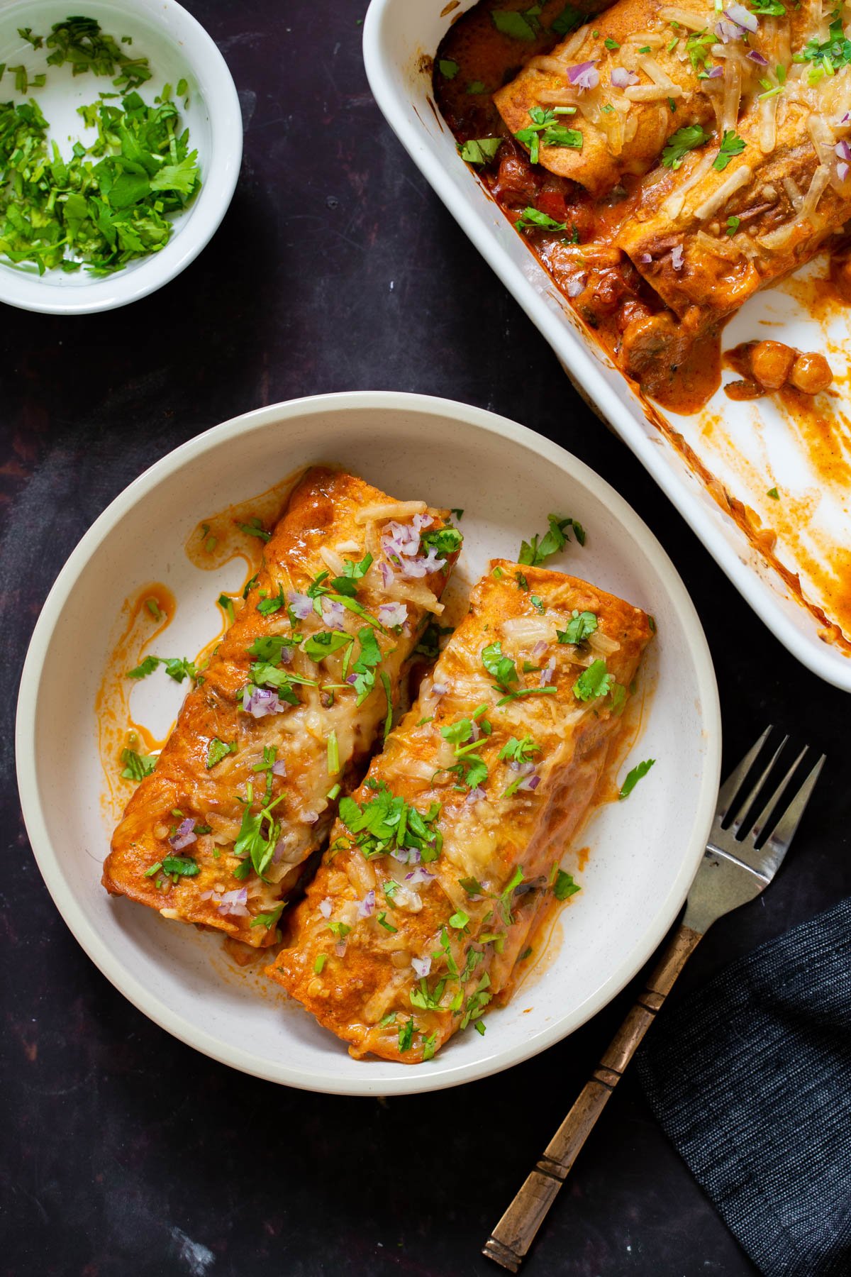 butter chicken enchiladas on the plate next to the baking pan