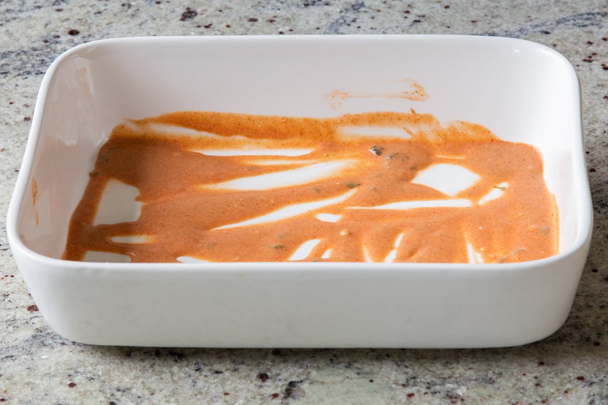 butter chicken sauce spread onto the bottom of a large baking dish