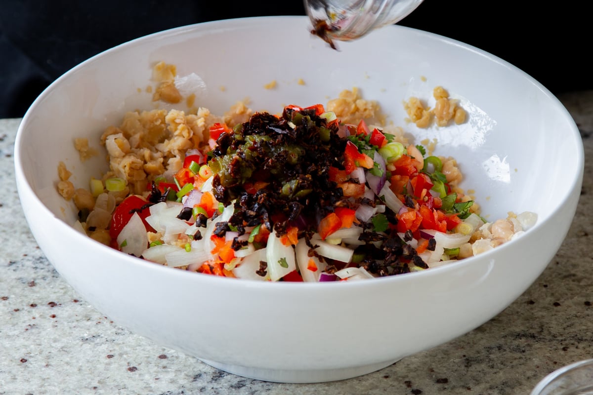 adding sun-dried tomatoes and spices to the bowl of mashed chickpeas and veggies