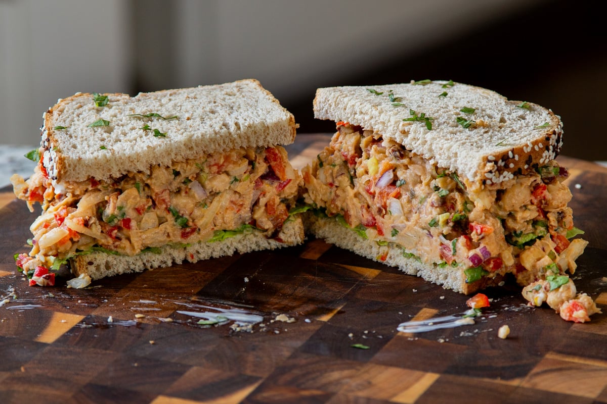 cajun chickpea salad sandwich sliced in half o a wooden cutting board