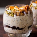 side shot of cannoli overnight oats in a glass topped with oranges, pistachios, and crispy cinnamon sugar tortilla pieces, so you can see the chocolate chips layer