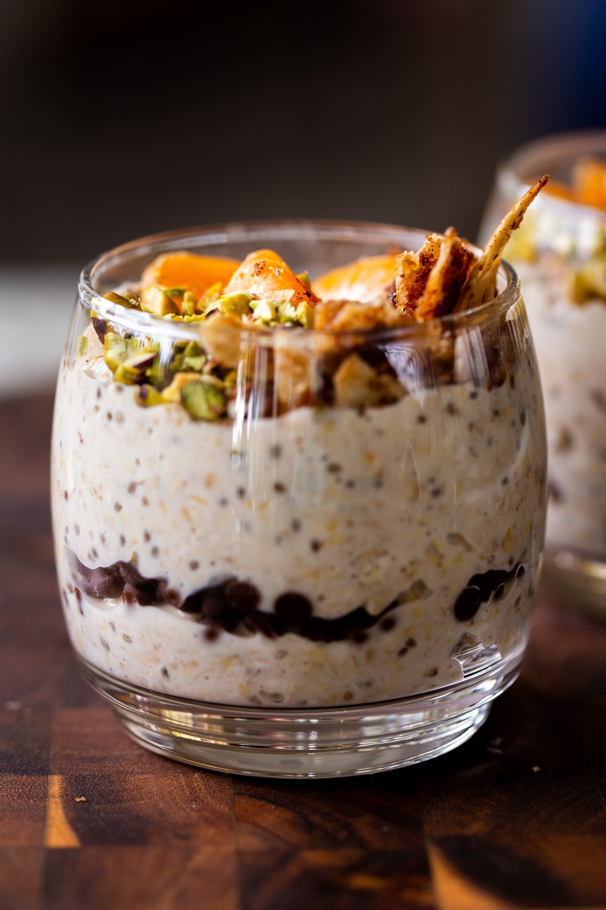 side shot of cannoli overnight oats in a glass topped with oranges, pistachios, and crispy cinnamon sugar tortilla pieces, so you can see the chocolate chips layer