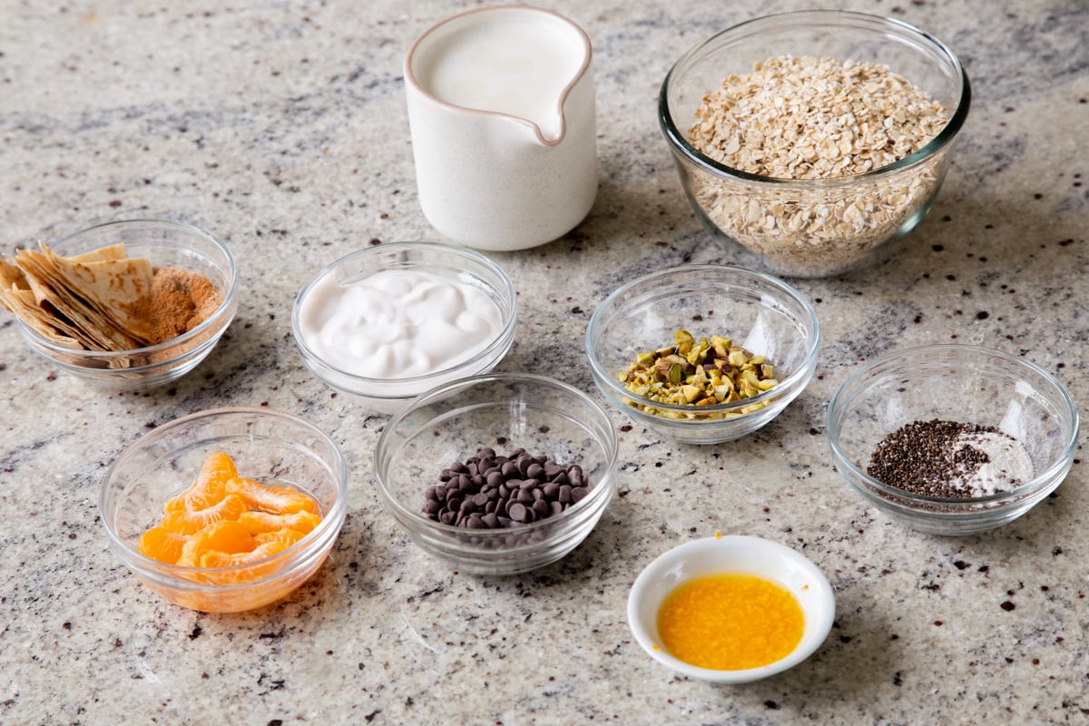 oats, chocolate chips, and other overnight oats ingredients in bowls on the kitchen counter