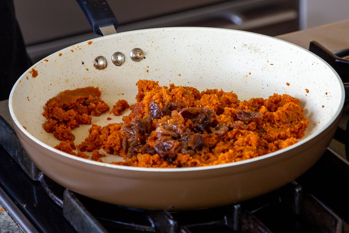adding raisins and flax meal to the pan of grated carrots