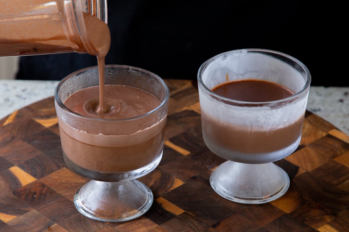 pouring mousse over the dark chocolate mixture in cups