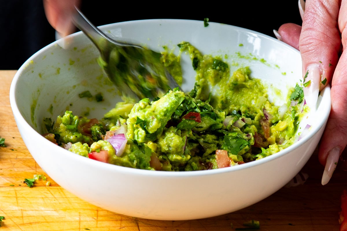 mixing the other guacamole ingredients into the avocado