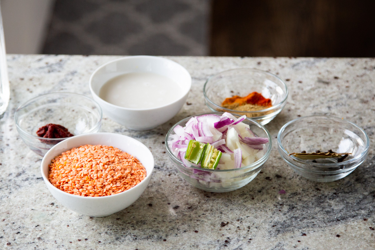 lentils, veggies, spices, and other dalcha ingredients in bowls on a kitchen counter