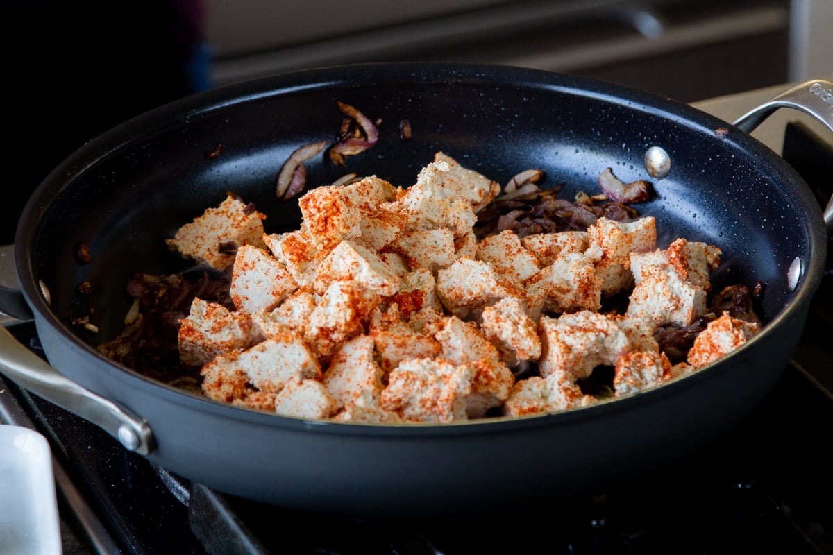 adding the spiced tofu to the pan with the onions