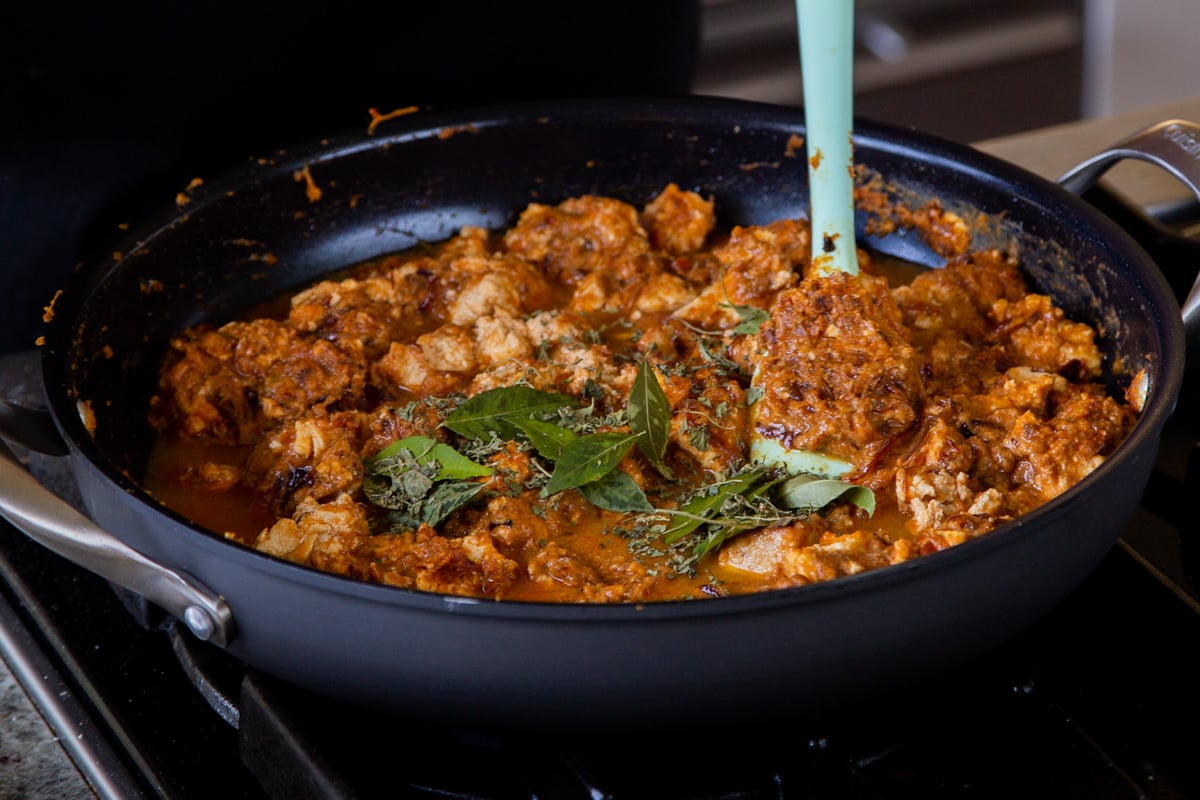 adding curry leaves and fenugreek to the Hyderabadi chicken curry in the pan