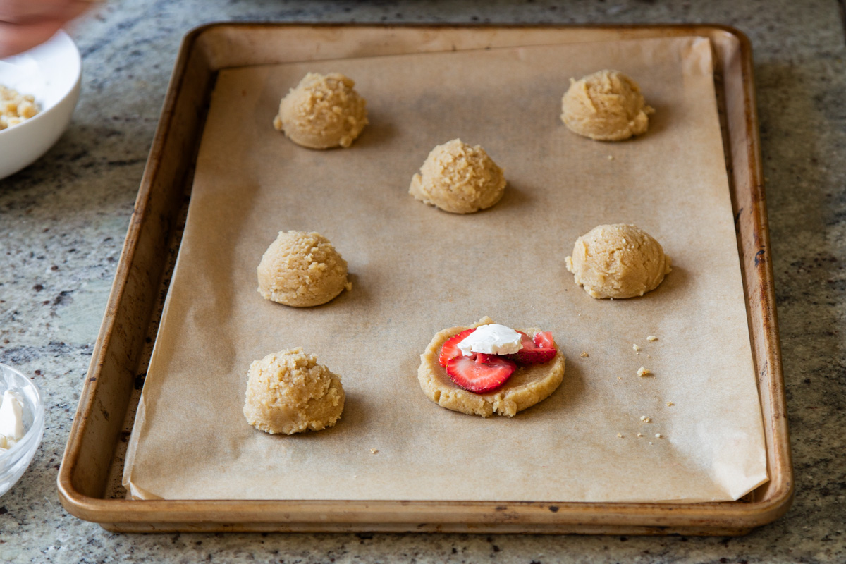 adding sliced strawberries and non-dairy cream cheese to a flattened piece of cookie dough
