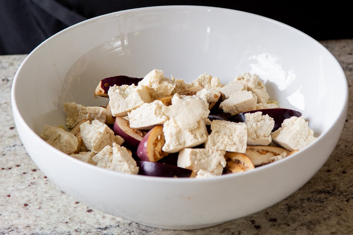 adding tofu and eggplant to the mixing bowl