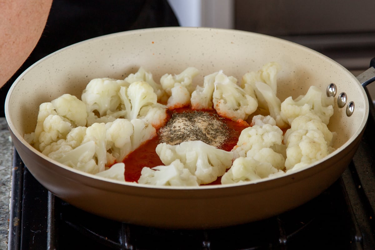 adding harissa paste and spices to the partially-cooked cauliflower