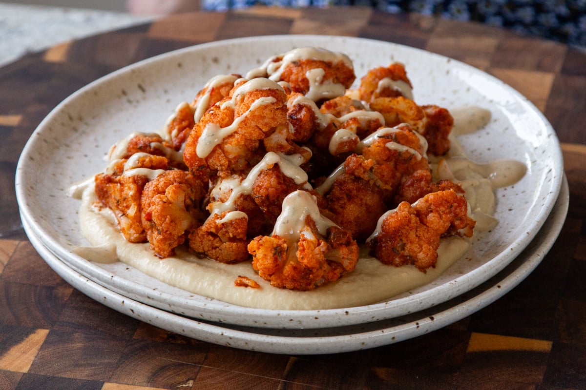 harissa cauliflower on a plate with hummus, and fresh herbs.