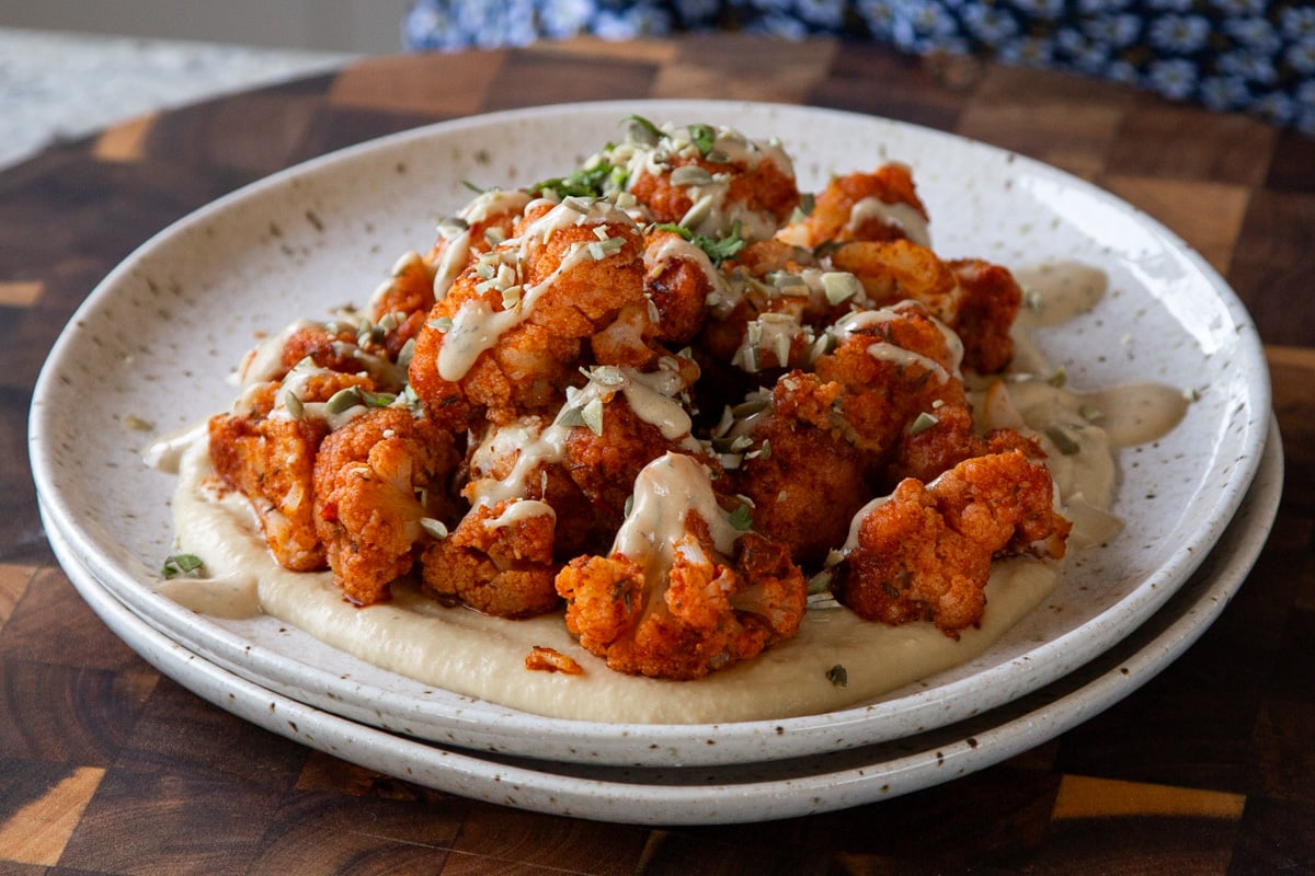 harissa cauliflower on a plate with tahini sauce, hummus, and fresh herbs.
