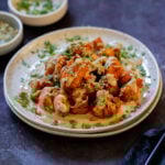 harissa cauliflower on a plate with tahini sauce, hummus, and fresh herbs.