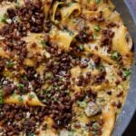 close-up of smoky skillet lasagna in the pan, topped with crispy lentils and fresh herbs