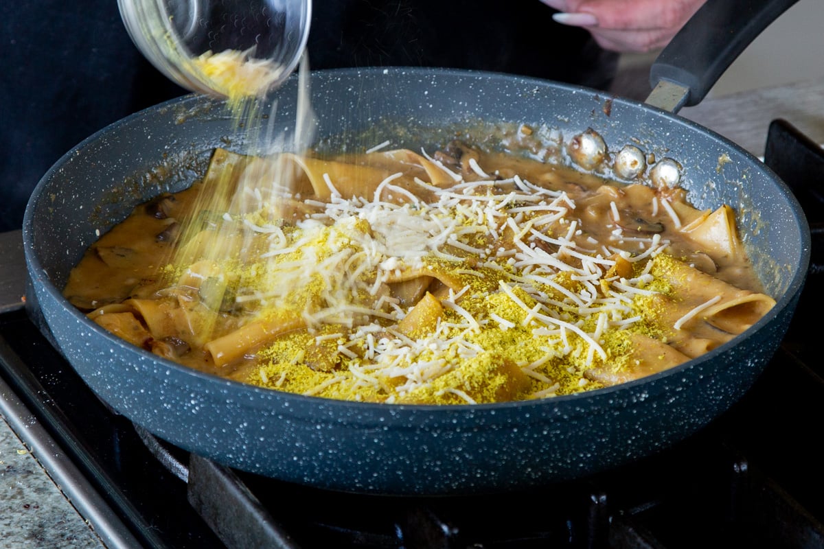 adding vegan parmesan and nutritional yeast to the pan of smoky skillet lasagna