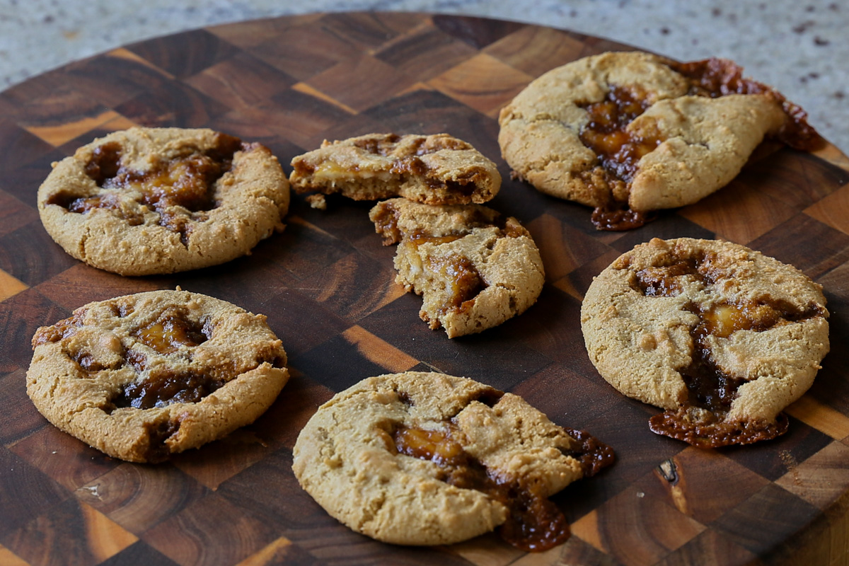 tiramisu cookies on a wooden cutting board, one cookie is broken in half, so you can see the inside
