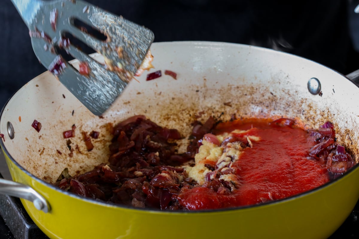 adding tomato to the pan of onions
