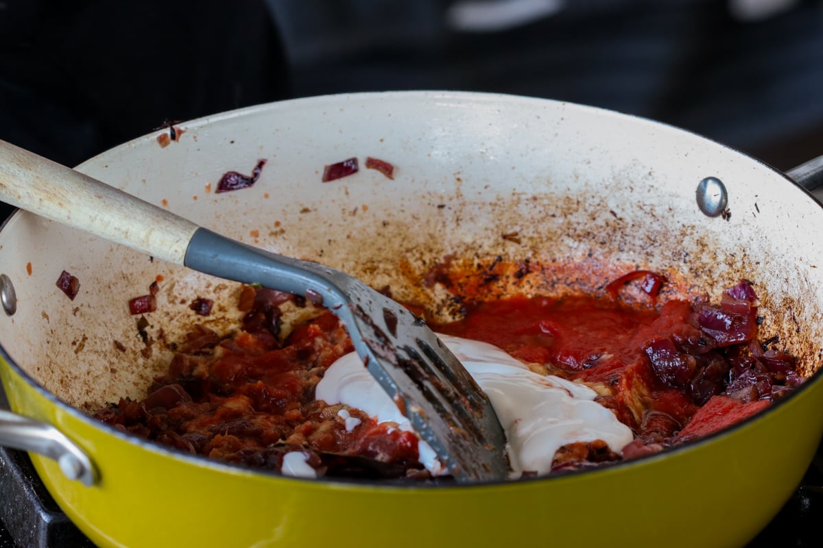 adding non-dairy yogurt to the pan of tomato and onion