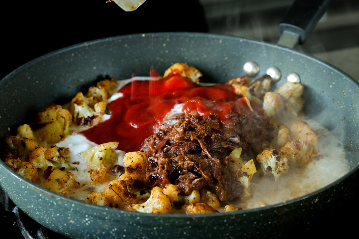 adding tomato puree and do pyaza sauce to cauliflower in the pan