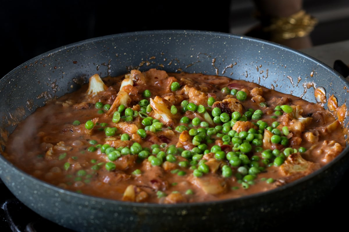 adding peas to the cooked cauliflower in the pan