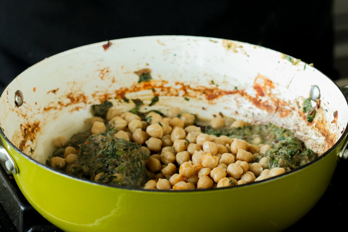 adding cooked chickpeas to the pan of creamy spinach