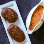 two mini chickpea loaves on a plate next to a gravy boat full of butter chicken sauce
