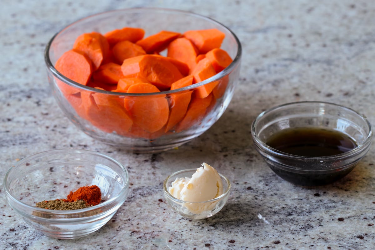 carrots, maple syrup, and spices in bowls on a kitchen counter