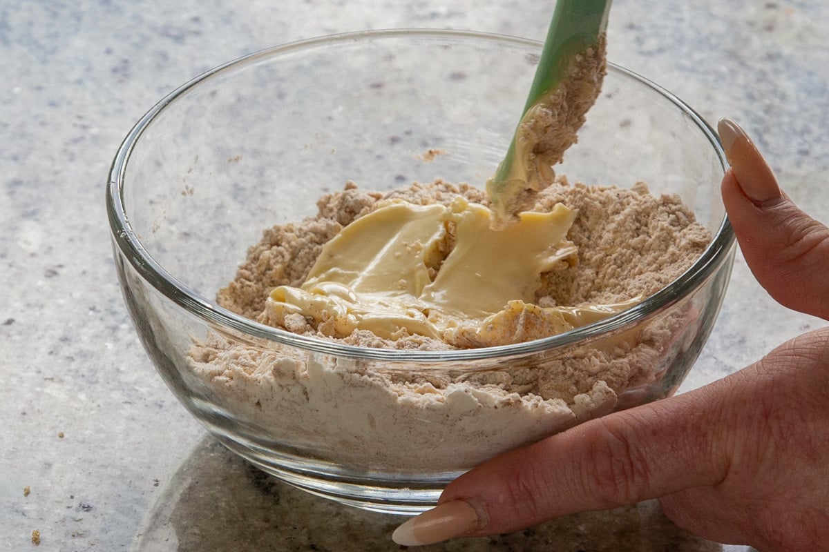 adding vegan butter to the bowl of vegan butter, oats, flour, and spices