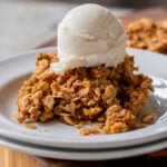 slice of pumpkin crisp on a white plate with ice cream on top