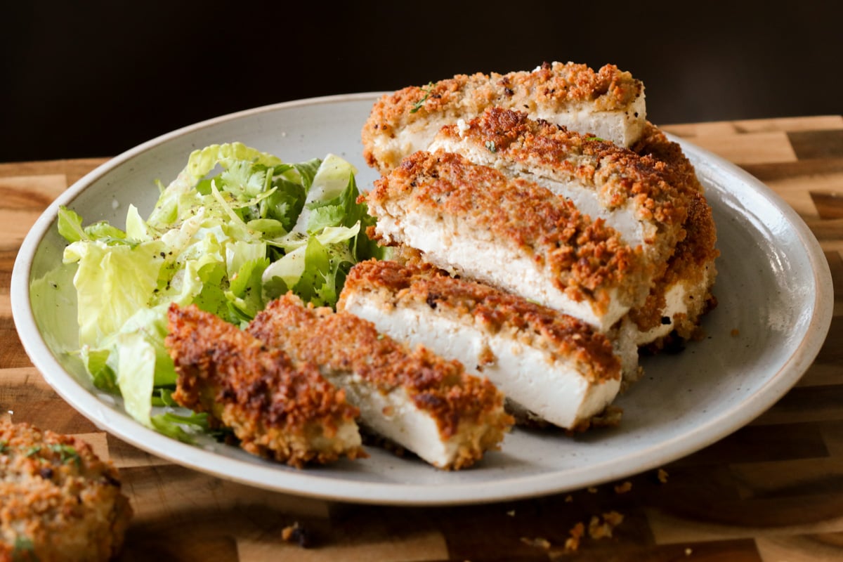 sliced vegan tofu schnitzel on the plate with a side salad