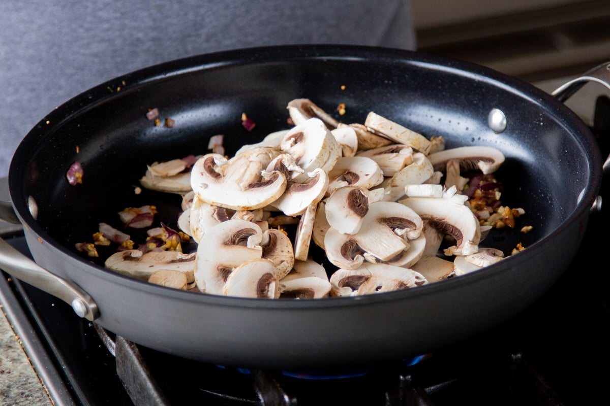 adding mushrooms to the pan of cooked aromatics