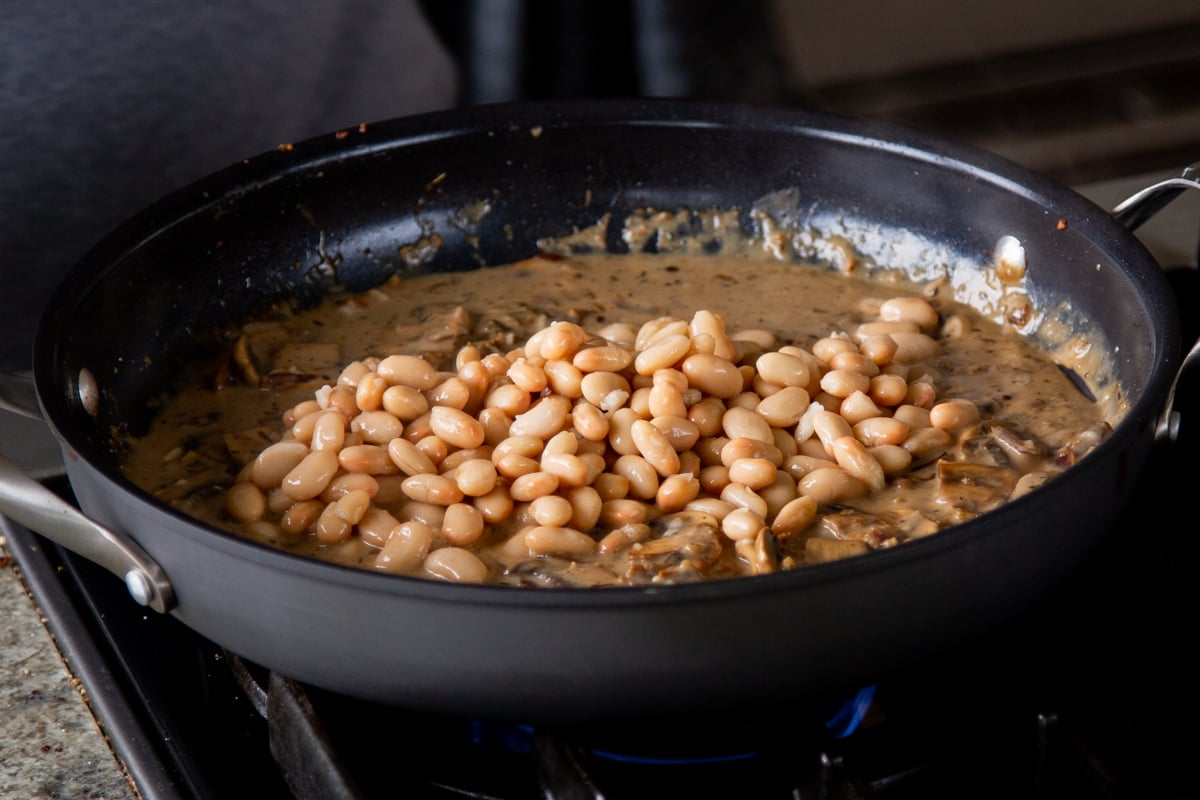 adding white bean to the pan of saucee
