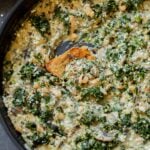 dipping a piece of bread into vegan white bean mushroom alfredo in the pan with spinach