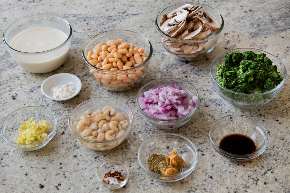 white beans, mushrooms, cashews, and other alfredo ingredients in bowls on a kitchen counter