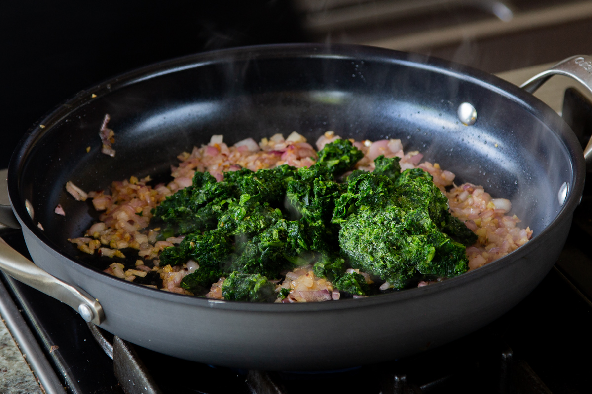 adding spinach to the cooked onions and garlic in the pan
