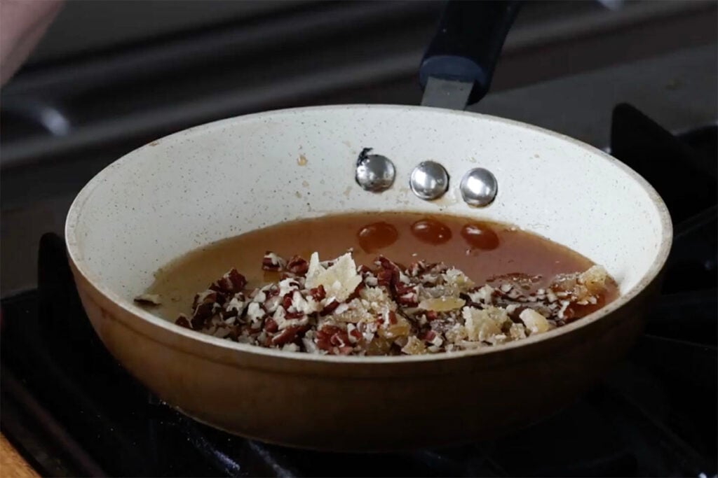 adding pecans and candied ginger to the pan of syrup