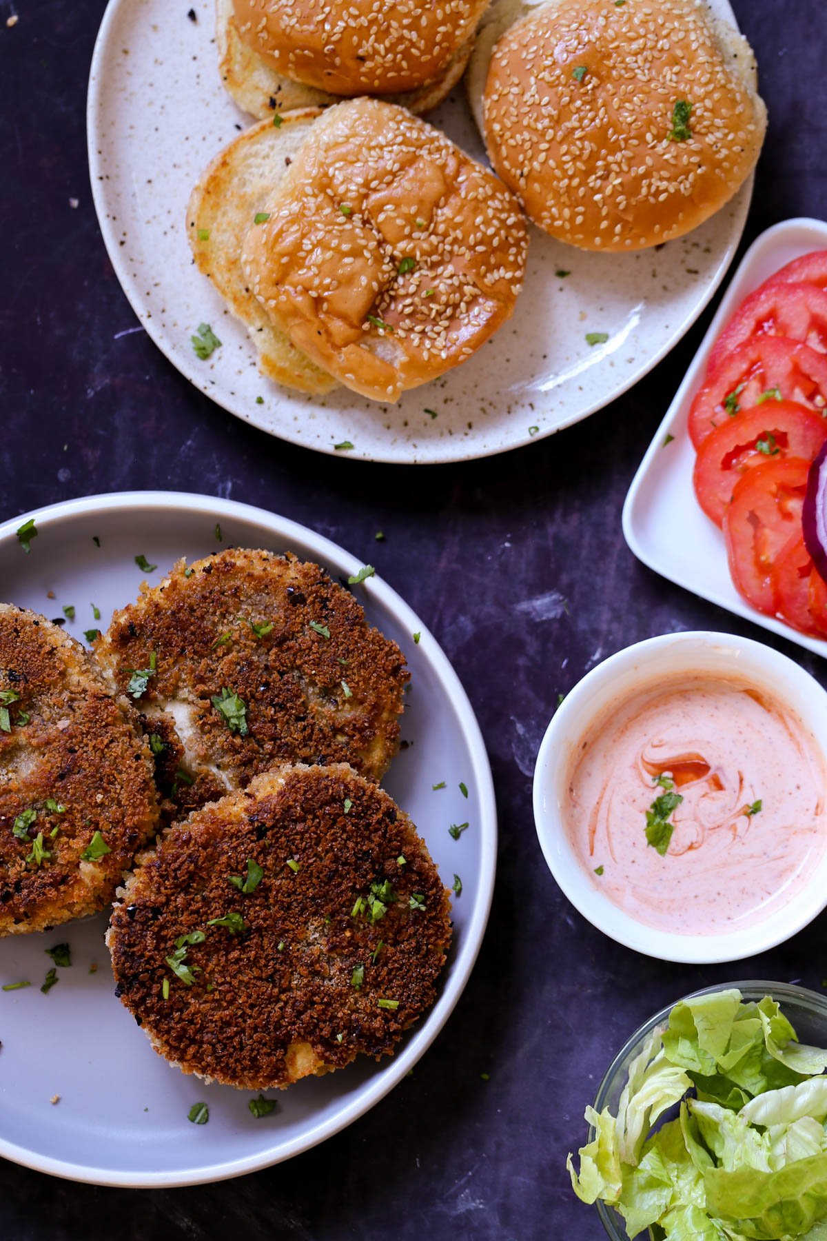 crispy vegan chicken patties on a plate with buns and toppings around them