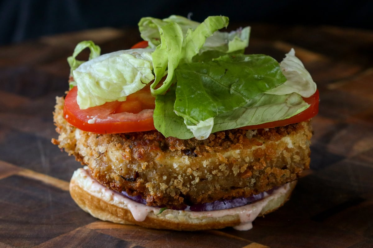 crispy vegan chicken patty, lettuce, onion, and tomatoes on the bun