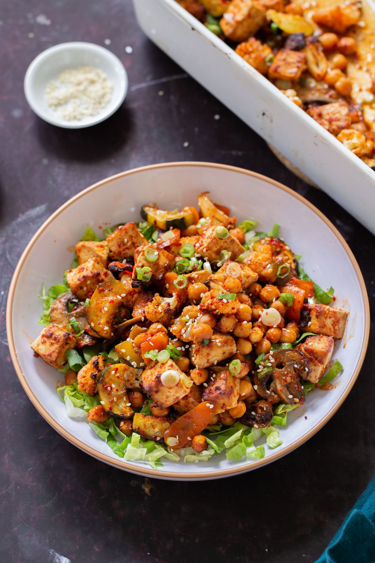 gochujang tofu and veggies in bowl over lettuce, next to the baking dish
