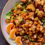 close-up of gochujang tofu and veggies in bowl over lettuce with orange pieces and sesame seeds